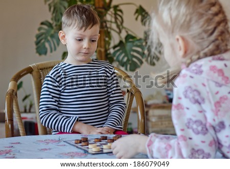 Cute little boy pulling a face and grimacing as he looks at the position of his pieces on a checkers board while playing a game with his sister