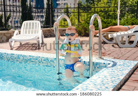 Small boy clambering out of a swimming pool onto the mosaic surround in his goggles and buoyancy jacket