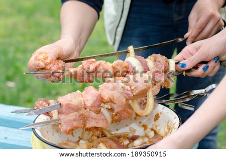 Closeup of the hands of a young woman preparing kebabs to grill on a BBQ threading spicy meat and onions from a basin onto metal skewers
