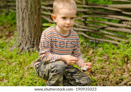 Little boy starting a campfire kneeling down on the ground with his matches in front of a small pile of leaves and wood