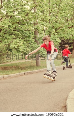 Athletic skilled young teenage girl roller skating on roller blades on a rural road as a young boy rides his scooter behind her