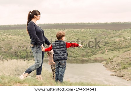 Little boy pointing to something in the countryside showing his mother a point of interest as they stand together on top of a grassy hill overlooking a steep valley and river