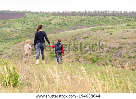 Mother walking with two small boys in the countryside holding their hands as they stride across a grassy hilltop on rolling hills above a river valley