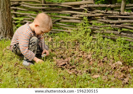 Young boy lighting a fire outdoors kneeling down in the grass striking a match against the box