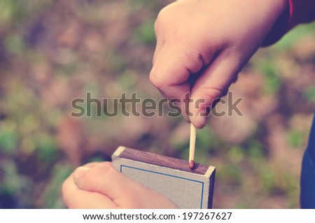 Child striking a safety match on a box of matches against a green grass background , close up of the hand