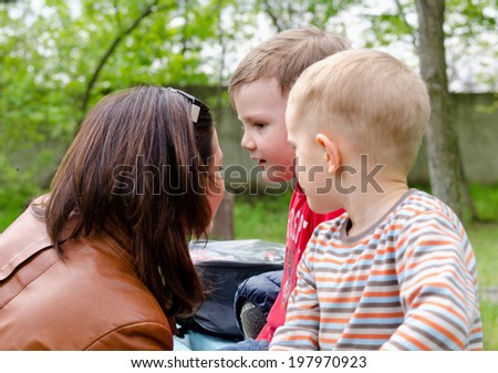 Attractive stylish young woman with her sunglasses on top of her head chatting to two small boys outdoors in a park, close up view of their faces