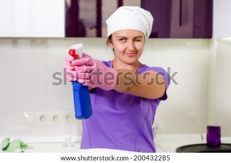 Playful housewife wearing a white cap over her long hair taking aim with the detergent pointing the spray bottle while aiming