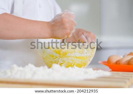 Little boy mixing cake ingredients in a mixing bowl whipping the flour and eggs to make the dough