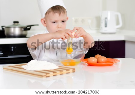 Young boy earning to be a chef breaking eggs into a mixing bowl with a look of concentration as he follows the recipe in his chefs uniform