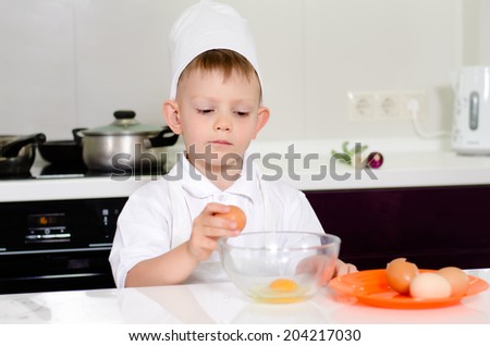 Young boy earning to be a chef breaking eggs into a mixing bowl with a look of concentration as he follows the recipe in his chefs uniform