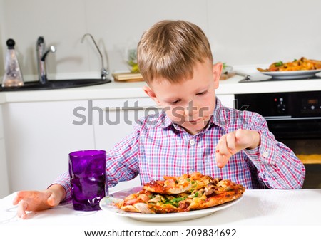 Little boy sitting at a table in the kitchen eating a big plate of homemade Italian pizza with a delicious golden crust