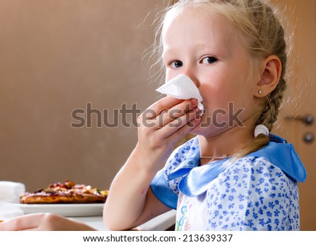 Pretty little girl sitting at the dinner table eating homemade pizza wiping her mouth with a napkin while turning to glance at the camera with a serious expression