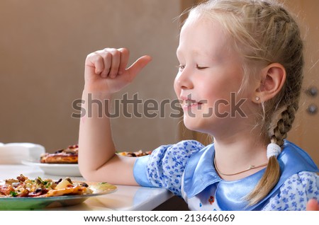 Pretty little girl sitting at the dinner table eating homemade pizza wiping her mouth with a napkin while turning to glance at the camera with a serious expression