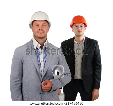 Two architects in partnership posing for the camera with the leader or boss in front with a stern expression and a polite junior partner behind doffing his hardhat in greeting, on white