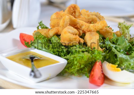 Battered deep fried calamari on a bed of fresh leafy green lettuce with a savory sauce served as a delicious seafood appetizer or meal