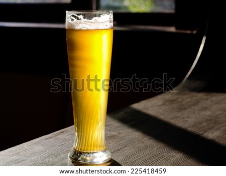 Ice Cold Beer on Classic Tall Glass Placed on Vintage Wooden Table Near the Window at the Bar.
