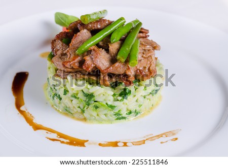 Gourmet Tasty Well- Cooked Beef Meat and Green Beans on Risotto Main Dish. Prepared on White Round Plate with Utensils on Sides.