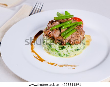 Gourmet Tasty Well- Cooked Beef Meat and Green Beans on Risotto Main Dish. Prepared on White Round Plate with Utensils on Sides.