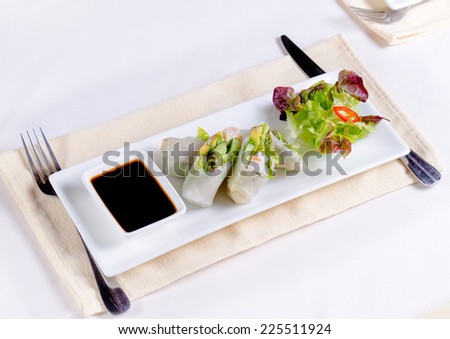 Gourmet Fresh Spring Rolls Cuts with Soy Sauce and Lettuce on White Rectangular Plate. Served on White Table.