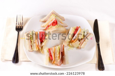 Small Cuts of Ham Sandwich with Cheese and Fresh Veggies on White Plate. Served on the Table with Fork and Knife.