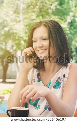 Attractive woman chatting on a mobile phone in her garden while stirringa cup of delicious coffee