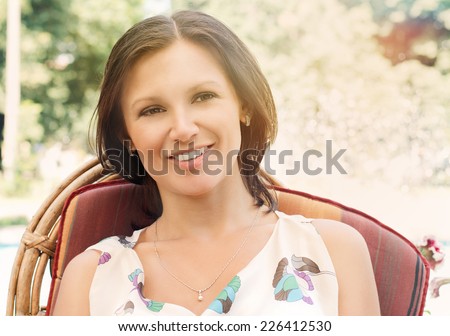 Smiling young brunette woman sitting in a comfortable garden chair enjoying the summer weather under the shade of a tree
