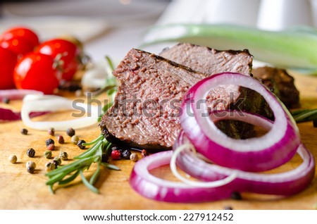 Sliced portion of rare roast beef with red onion rings seasoned with peppercorns and fresh rosemary