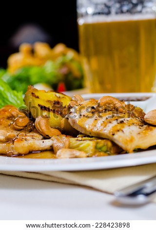 Close Up of Pineapple Cashew Chicken Dish on Plate Served with Glass of Beer in Restaurant