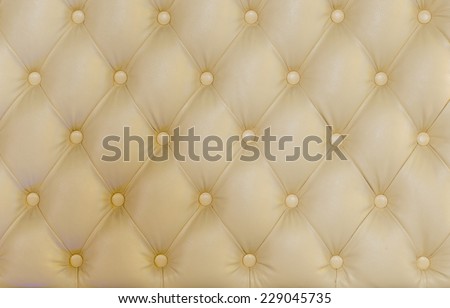 Button back upholstery detail on cream colored textile or leather showing the diamond pattern created by the buttons, full frame