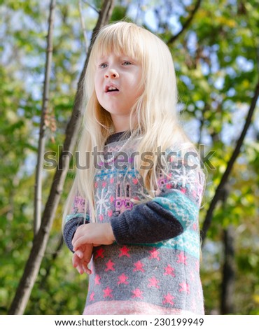 Close up Pretty Little Girl, with Long Blond Hair, Wearing Autumn Fashion Outfit at the Woodland with Tall Trees Background.