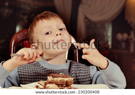Contented little boy eating a large slice of creamy cake for dessert as he sits smiling with pleasure at the dining table