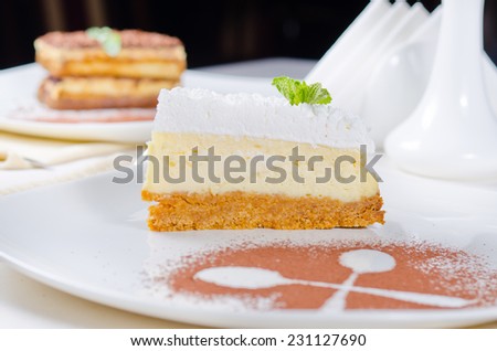 Freshly baked delicious slice of cheesecake with a biscuit base topped with cream presented on a plate with crossed spoon outline in chocolate powder