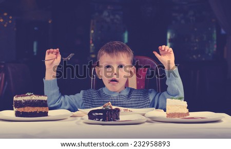 Cute young boy celebrating his birthday with a line up of different cake in front of him pulling a comic face as he tries to make up his mind where to begin eating