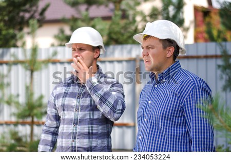 Two Male Project Engineers in White Helmets and Checkered Long Sleeve Shirts, Monitoring the Project Site Seriously.