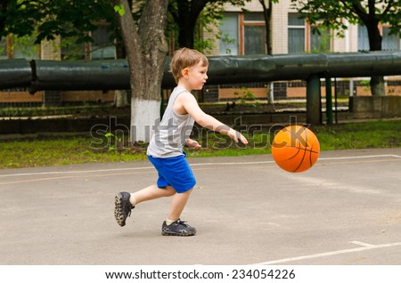 Little boy playing basketball running along the court in his sports wear bouncing the ball, side view outdoors