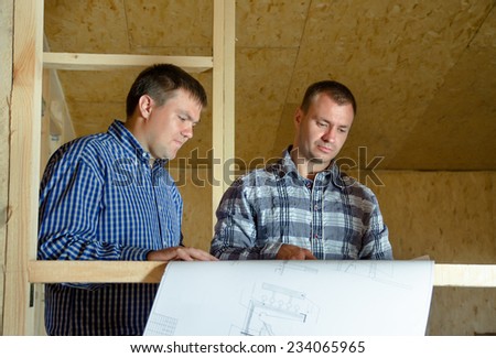 Two builders discussing a building plan as they stand in the interior of a new build timber frame house still under construction
