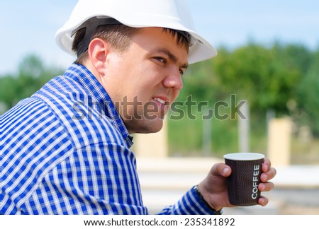 Close up side view of the face of a young builder in a hardhat sitting on a building site taking a coffee break