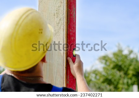 Builder ensuring that a beam is vertical holding a builders level against the wooden panel as he installs it on a new building during construction