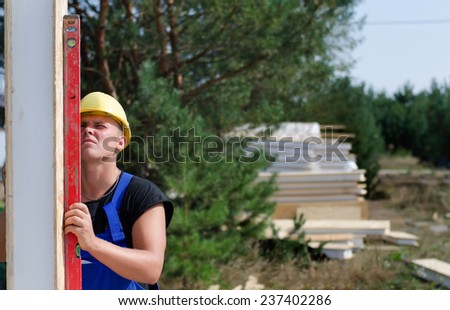 Builder using a builders level against an upright wooden insulated wall panel to ensure it is vertical