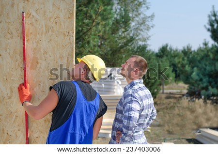 Builder and engineer checking a wooden wall panel using a level to see that it is in a vertical position on a residential building site