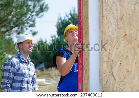 Two builders installing insulated wooden wall panels on site checking with a builders level to see that they are vertical