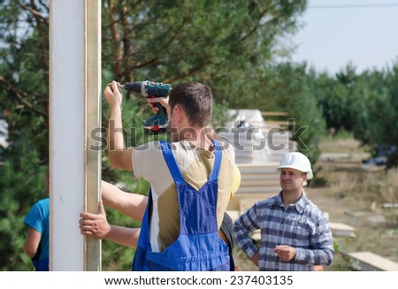 Team of builders installing insulated wall panels on a residential building site watched by the architect, engineer, or foreman