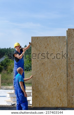 Two builders installing wooden wall panels on a residential building site aligning the new panel in the vertical position
