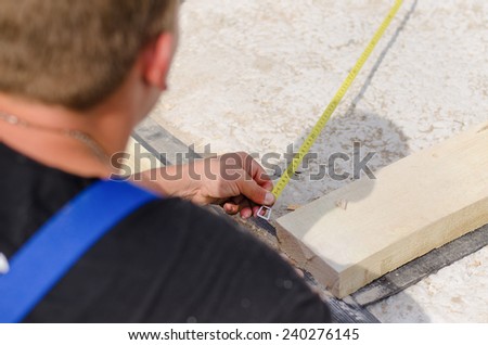 Over the shoulder view from above of a workman or builder measuring a diagonal of the new floor with a tape measure
