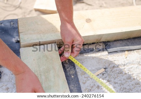 Hands of a carpenter taking a diagonal measurement on a new build building site as he aligns to wooden corner beams