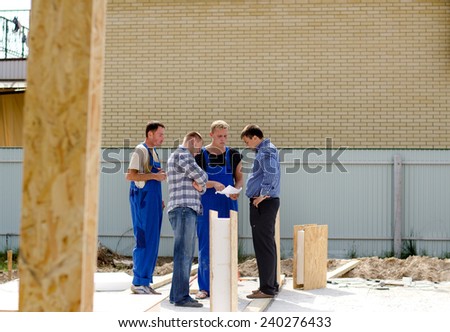 Group of builders having a meeting on site standing grouped around an insulated wooden wall panel discussing a paper document