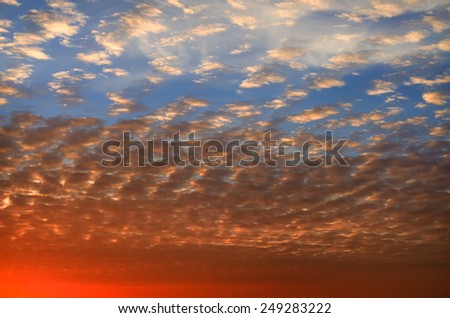 Spectacular orange sunset over the horizon in a blue sky with scattered small white clouds glowing with color