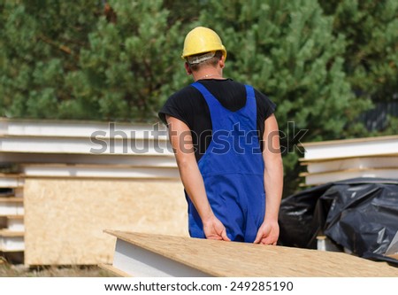 Builder walking away from the camera carrying an insulated wall panel in his hands behind his back