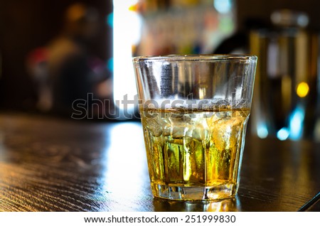 Close up of a tumbler or glass of whiskey or brandy on a wooden bar counter backlit by light from a window