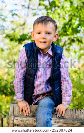 Happy attractive little boy climbing over a wooden fence or gate with a joyful smile outdoors in woodland